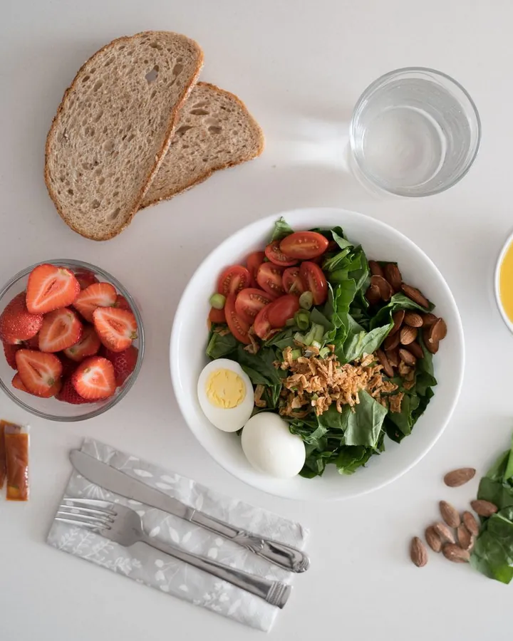 Vue du dessus : un bol de salade, des fraises, du pain complet et un verre d’eau
