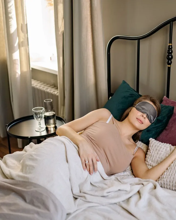 Une femme dort, un masque sur les yeux ; sur la table de chevet, seulement un verre d’eau